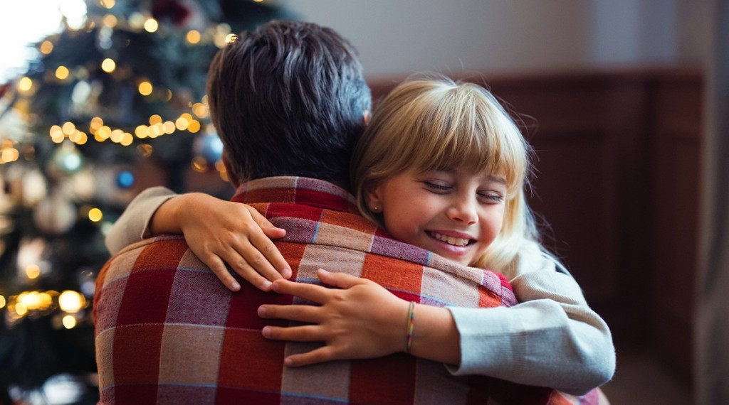 Father hugs young daughter next to a Christmas tree