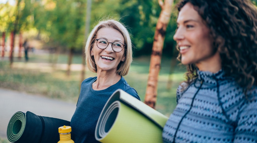 Two women walking in nature with yoga mats.